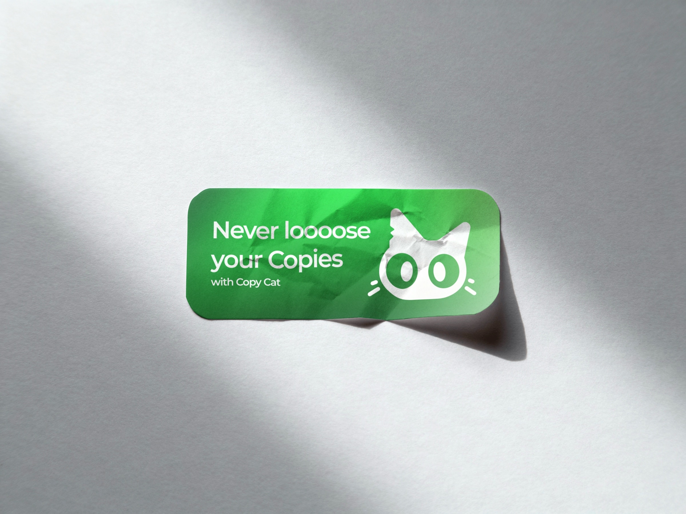 A green Copy Cat sticker on white paper in raking light, carrying the line about never losing your copies beside the cat face