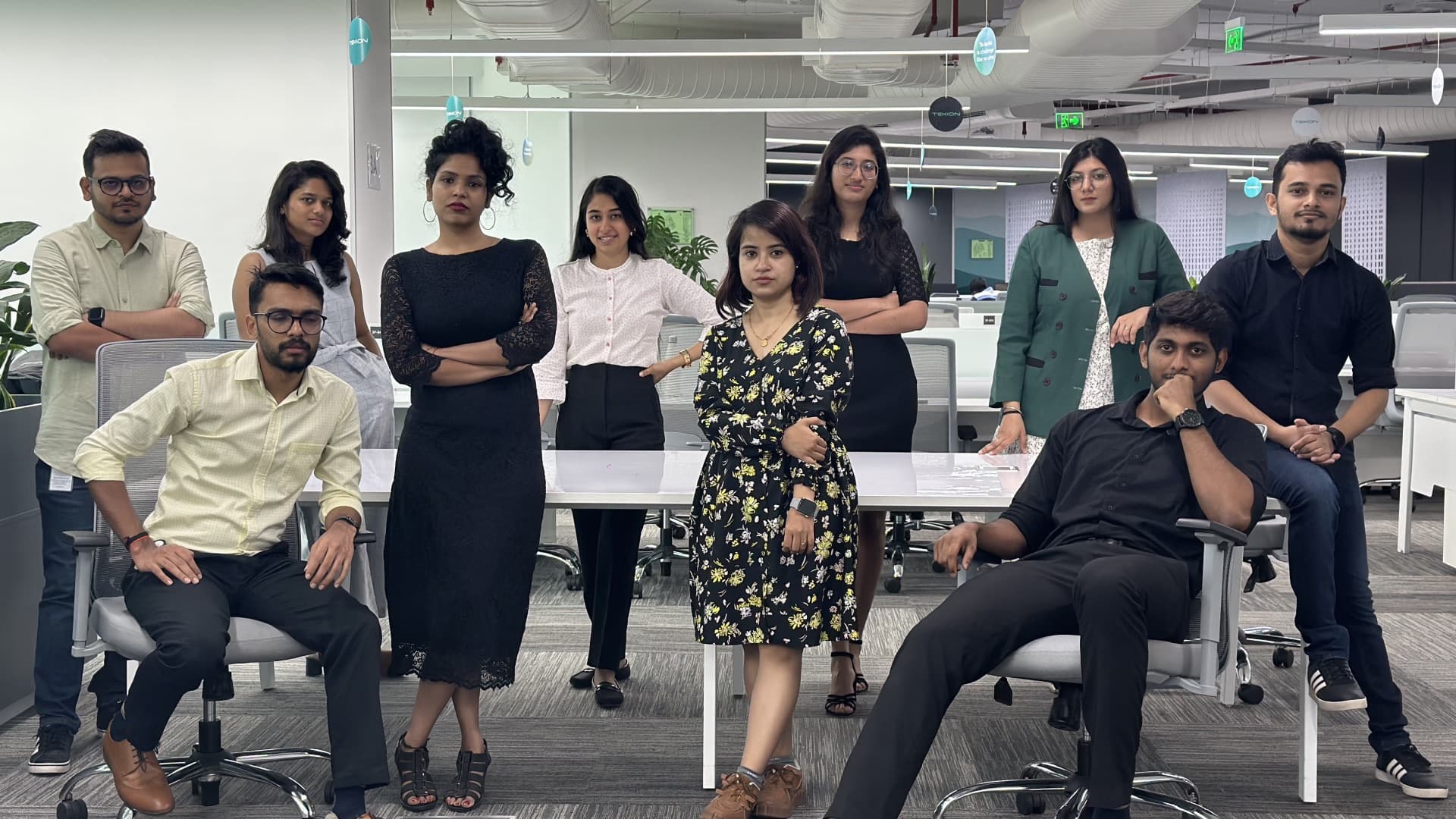 A group posed around the desks in the Tekion office, some standing and some seated in office chairs.